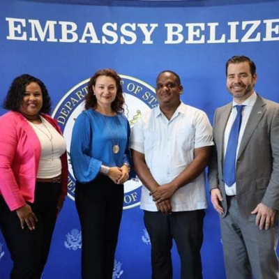 Men and women standing in front of a banner bearing the caption Embassy Belize.